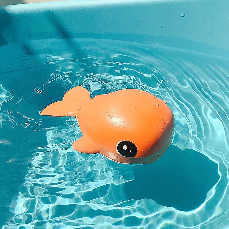 Orange whale-shaped children bathing toy floating in water, made of plastic, clockwork function.