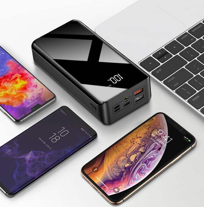 30000mAh power bank with LCD display charging multiple devices next to a laptop.